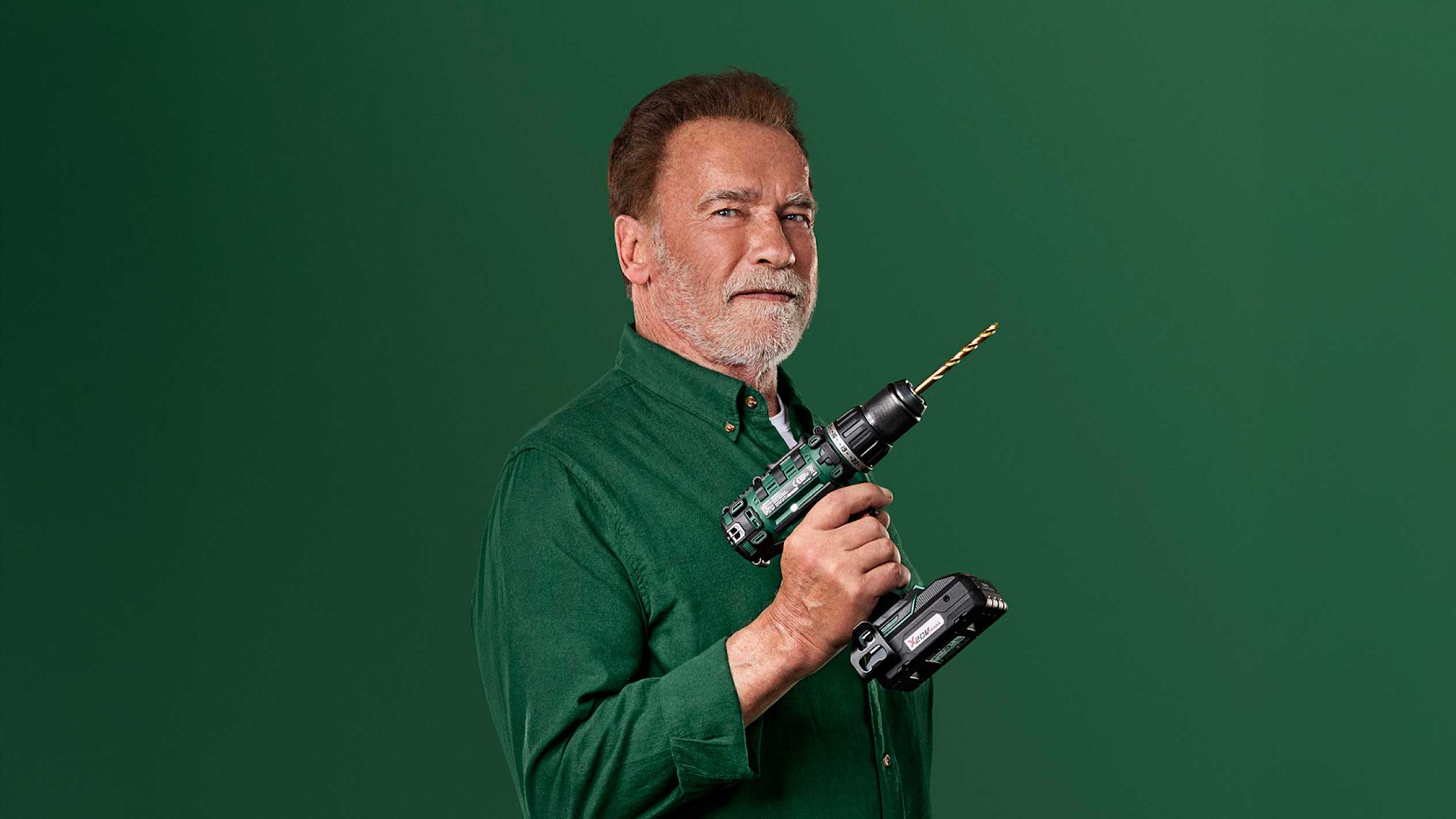 Arnold Schwarzenegger segurando uma furadeira sem fio verde com uma broca dourada.