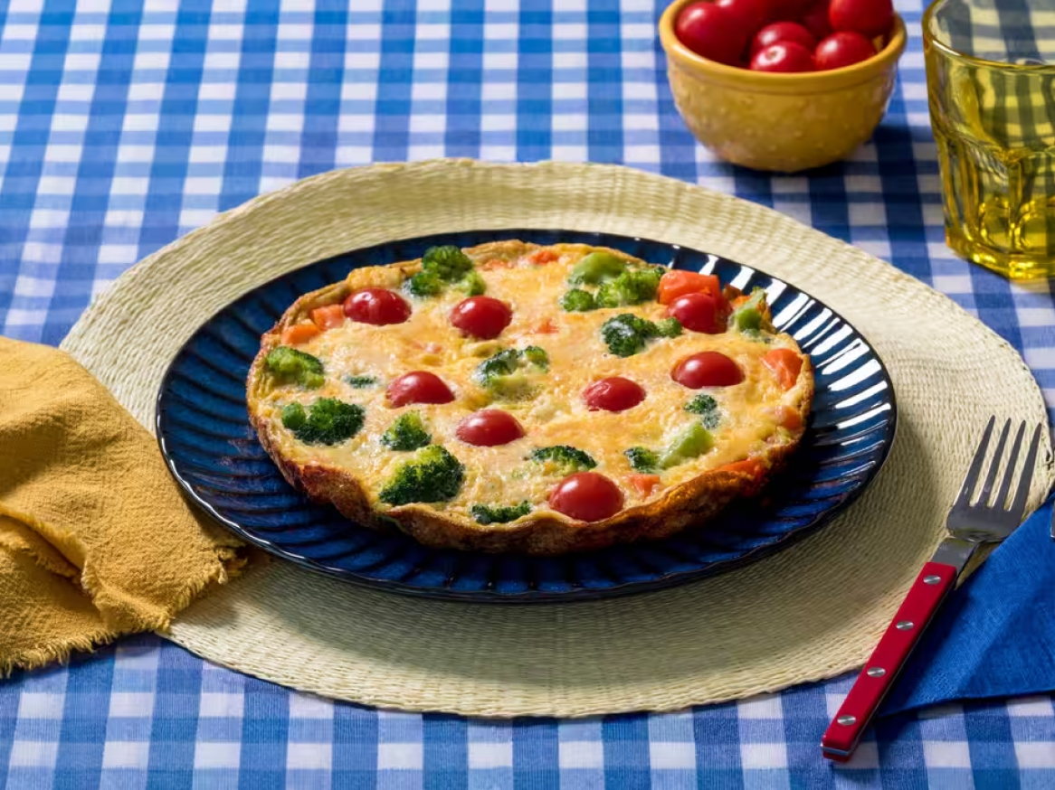 Quiche de brócolos, tomate cereja e cenoura numa mesa com toalha de xadrez azul e branco.