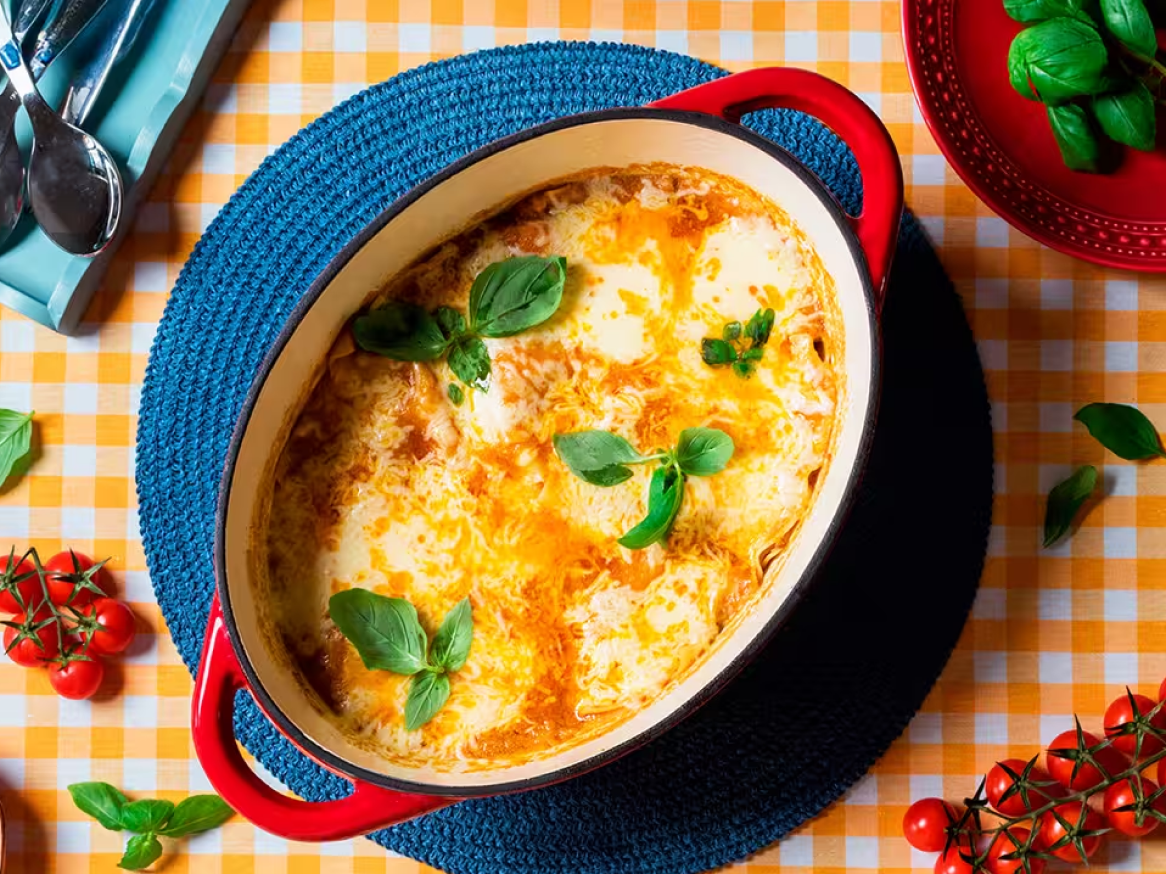 Lasagna assada com queijo derretido e manjericão fresco numa travessa vermelha.
