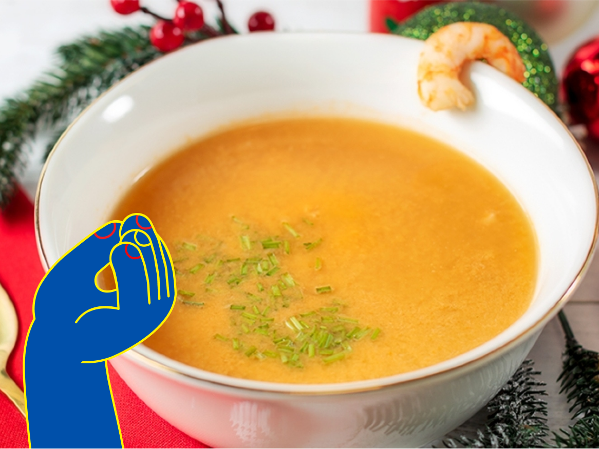 Sopa cremosa de camarão em uma tigela branca, decorada com ervas e um camarão.