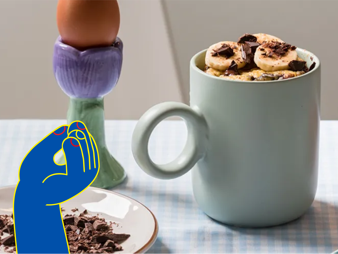 Mug cake de banana com chocolate em uma caneca, acompanhado de um ovo em um suporte de ovos.