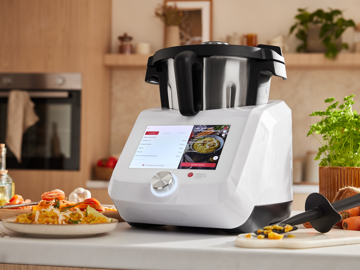 Monsieur Cuisine Smart, processador de alimentos multifuncional, na cozinha, com receita de Curry exibida na tela.