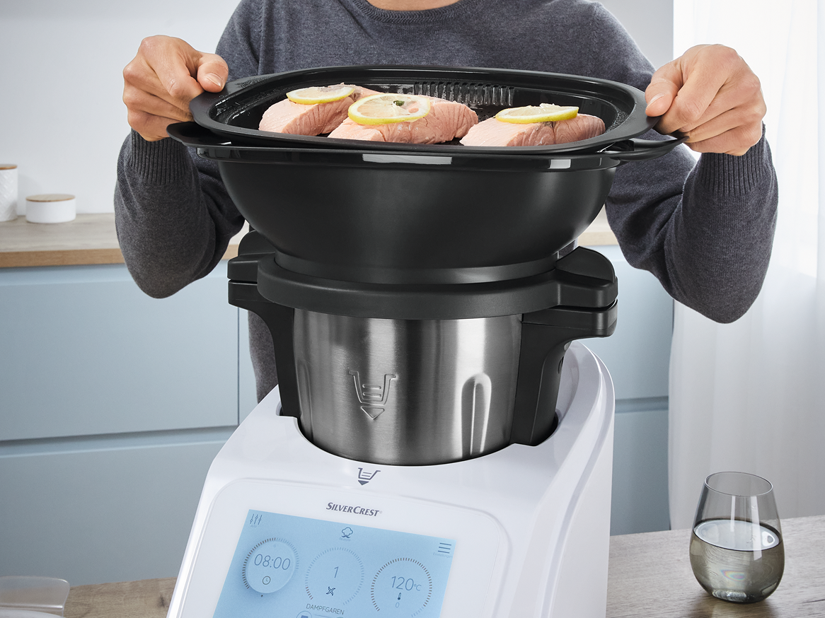 Uma pessoa coloca um cesto de vapor com salmão numa panela de pressão SilverCrest.