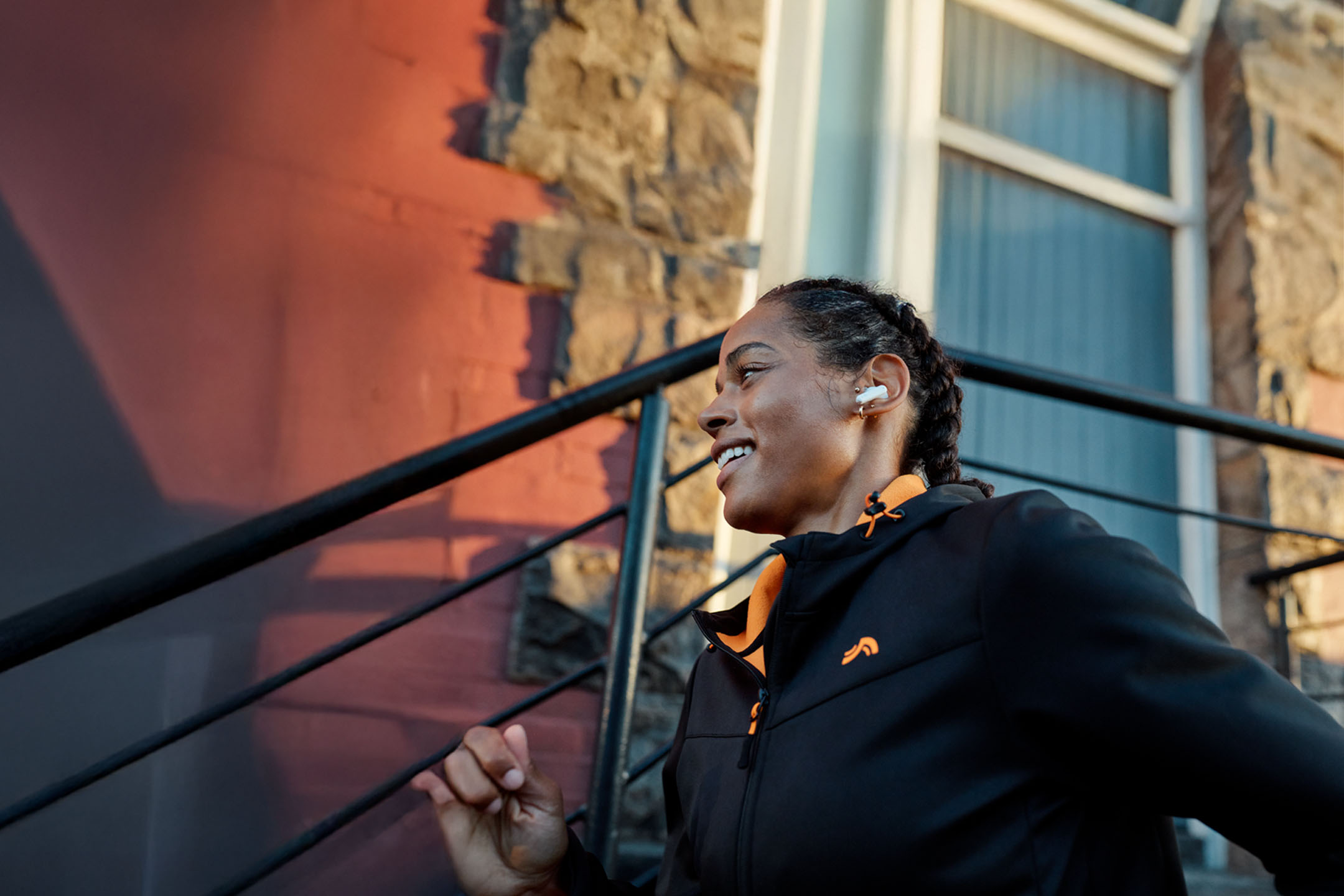 Mulher correndo com fones de ouvido, vestindo jaqueta.