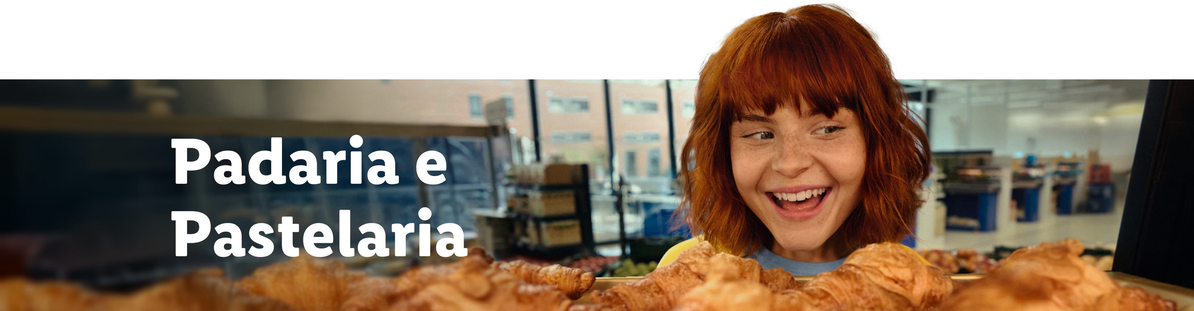 Mulher ruiva sorridente olhando para croissants frescos em uma padaria.