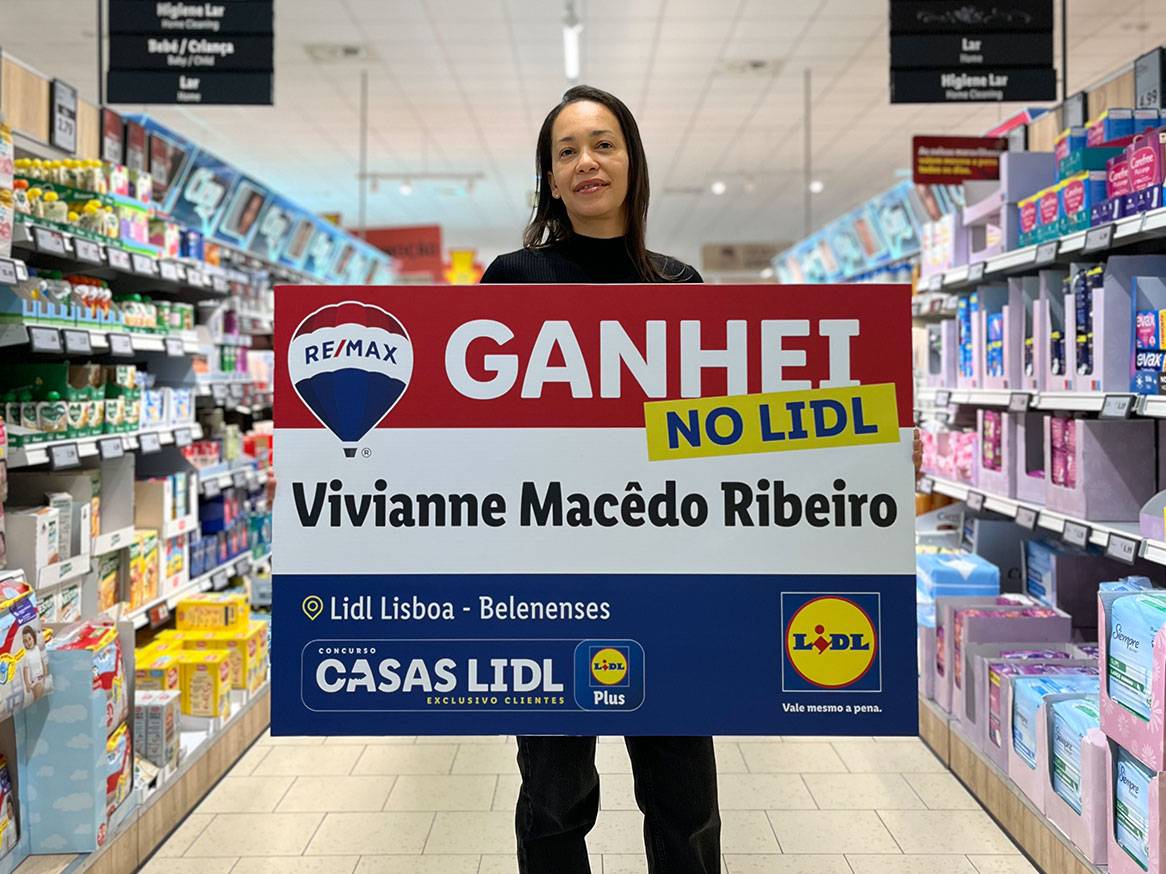 Mulher sorridente segura cartaz 'GANHEI NO LIDL' com o seu nome, em corredor de supermercado.