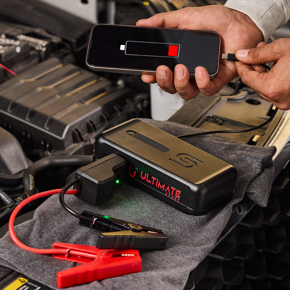 Powerbank de arranque para automóvel Ultimate Speed com cabos de ligação e smartphone ligado para carregamento.