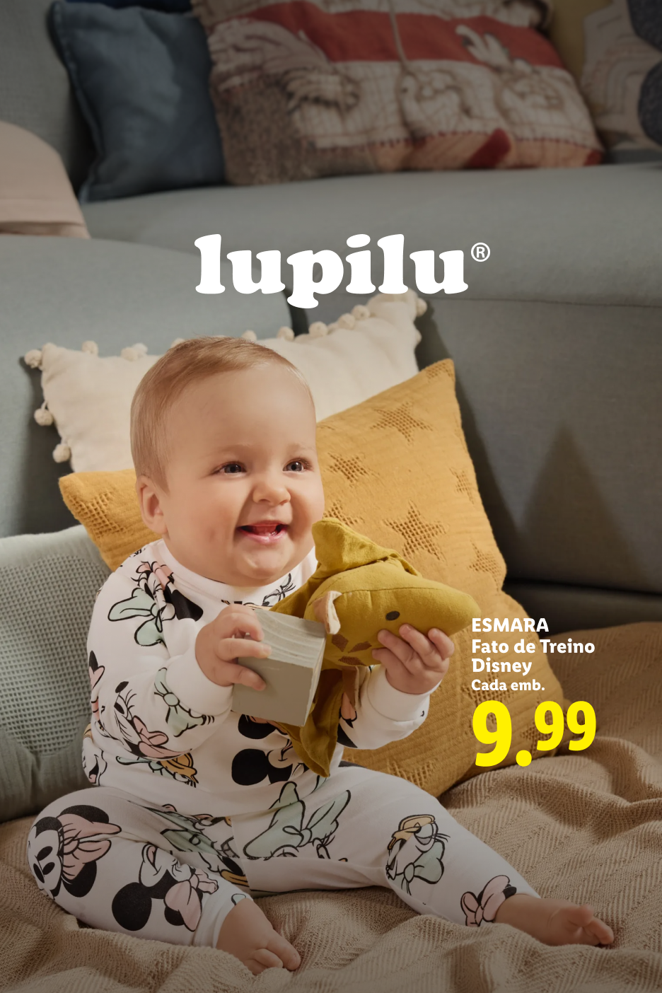 Bebé sorridente em pijama com padrão Disney, segurando um brinquedo e um bloco. Preço: 9,99.